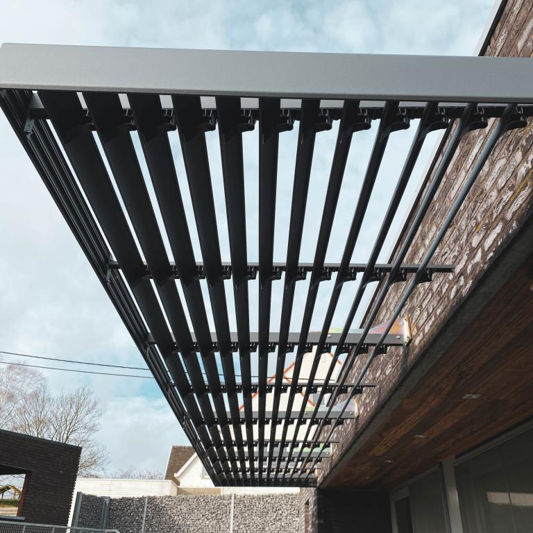 Renson Sunclips structurele zonwering geplaatst aan deze gerenoveerde woning te Anzegem. De aluminium lamellen passen naadloos bij het hout van de gevelbekleding. Een modern en strak design