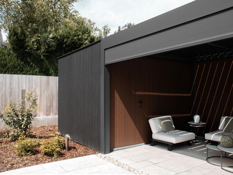 Renson Camargue terrasoverkapping geplaatst door Demaeght zonwering te Dilbeek. Een aluminium pergola gecombineerd met een houten tuinberging met zwart gelakte houten profielen. Combo tussen berging en outdoor living. Design architectuur tuin terras inspiratie offerte West-vlaanderen Oost-vlaanderen Deinze Kortrijk Tielt Roeselare Brugge Oudenaarde Kluisbergen Ronse Dilbeek Brussel Leuven