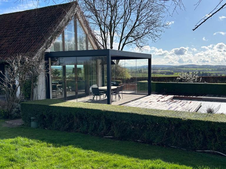 Renson Camargue lamellendak geplaatst door Demaeght zonwering te Doornik. Een aluminium pergola gemonteerd aan de woning. Schuifglas en geïntegreerde zonwering. Ook led-verlichting alsook een Lineo Fix lamel met een Heatsail verwarming eraan. Deinze Waregem Kortrijk Ronse Kluisbergen. Vraag hier uw vrijblijvende offerte op maat.